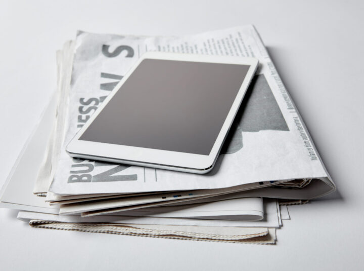 digital tablet with blank screen near business newspapers with articles on white